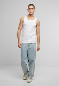White cotton tank top paired with light blue oversized jeans and cream sneakers, featuring a relaxed fit and standard stitching details.