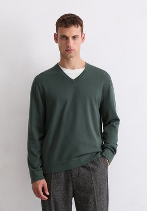 Pull vert à col en V en tricot doux, avec des manches longues et une coupe décontractée, associé à un pantalon gris texturé.