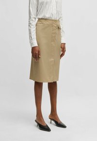 Khaki pencil skirt made of smooth fabric, featuring a side tie detail, knee-length cut, and a clean, tailored silhouette.