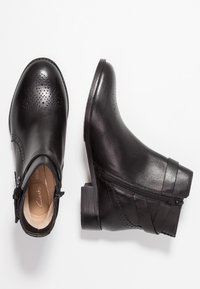 Svarta läderankelstövlar med perforerad detalj, sidoförslutning med dragkedja och staplad klack. Har en slät textur och diskreta remmar på sidan.