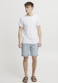 Bílé bavlněné tričko v kombinaci s světle modrými džínovými šortkami s ohrnutými lemy. Hnědé sandály doplňují ležérní outfit.