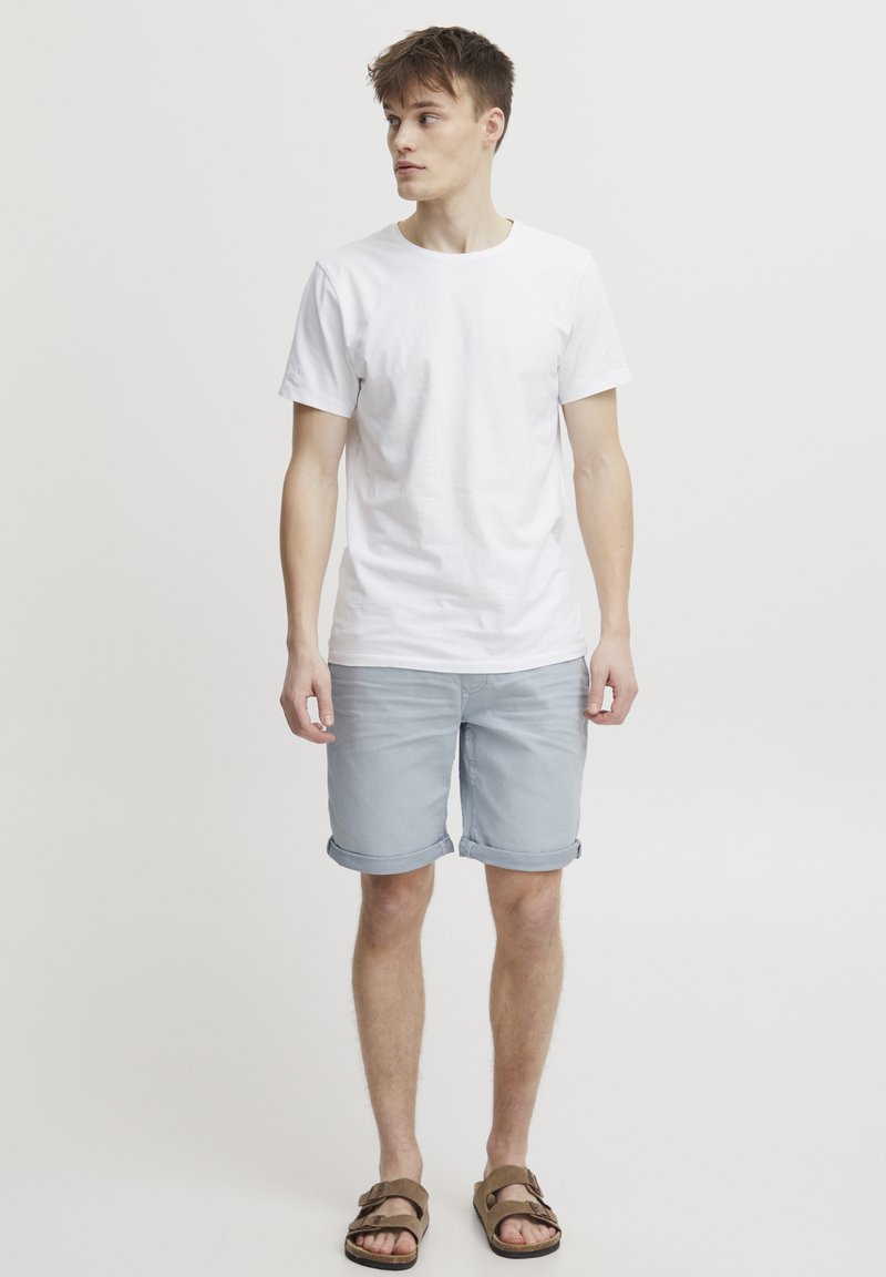 Bílé bavlněné tričko v kombinaci s světle modrými džínovými šortkami s ohrnutými lemy. Hnědé sandály doplňují ležérní outfit.