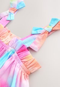 Vestido multicolor con tela de degradado pastel. Borde superior con volantes y tirantes con lazos en tonos rosa claro, azul y naranja.