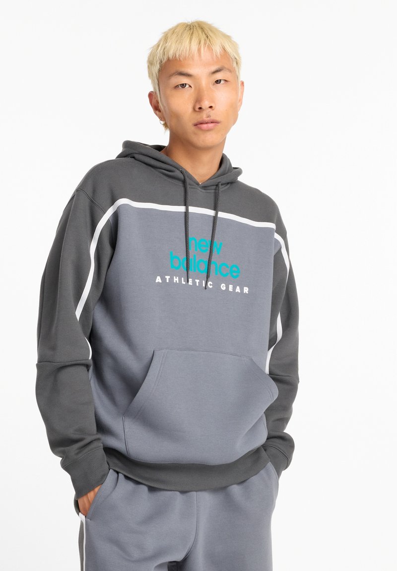 Sudadera gris con mangas en un gris más oscuro. Presenta texto de logo en turquesa "new balance ATHLETIC GEAR" y un bolsillo frontal. Tejido suave.