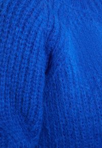 Tessuto di maglia blu con un motivo spesso e testurizzato, caratterizzato da punti variabili. Aspetto morbido, che suggerisce calore e comfort.