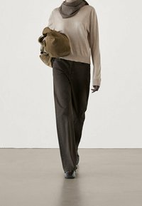 Beige gebreide trui met een grijze sjaal, losse zwarte spijkerbroek en een bruine tas. Soepele textuur, relaxte pasvorm en neutraal kleurpalet.