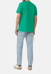 Zielona koszulka z krótkim rękawem i okrągłym dekoltem, połączona z jasnoniebieskimi dżinsami i codziennymi butami z beżowymi akcentami.