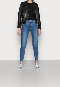 Chaqueta de cuero negra de motorista, top negro ajustado, jeans skinny azul claros y zapatillas plateadas. Diseño minimalista y texturas suaves.