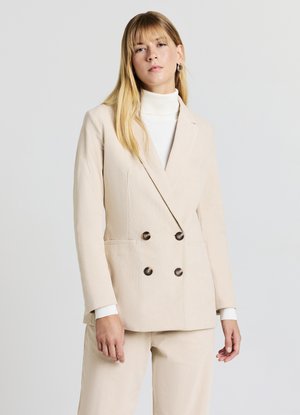 Blazer doppiopetto in corduroy beige con rever a punta e due tasche frontali. Presenta bottoni marrone scuro e una finitura liscia e testurizzata.