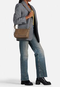 Brun læder crossbody taske med en struktureret overflade, minimalistisk design og justerbar rem, parret med grå blazer og flagrende jeans.
