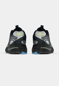 Μαύρα αθλητικά παπούτσια με υφή στο επάνω μέρος, διαφανή στοιχεία και πράσινες λεπτομέρειες. Διαθέτουν μαλακή σόλα και ενισχυμένο πίσω μέρος στη φτέρνα.