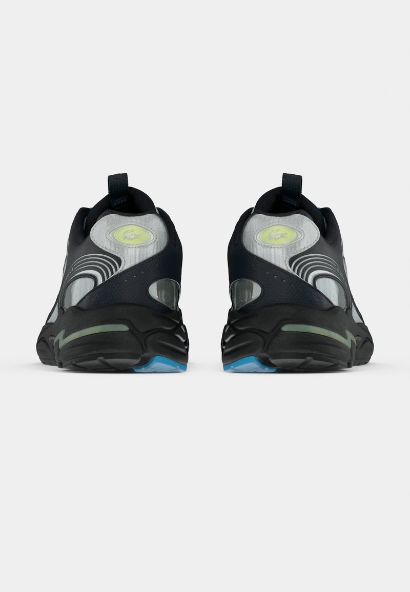 Chaussures de sport noires avec une tige texturée, des accents translucides et des détails verts. Dotées d'une semelle rembourrée et d'un talon renforcé.