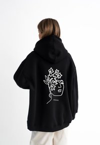 Felpa nera con un grande disegno bianco di un volto e fiori sul retro. Presenta un cappuccio e una vestibilità comoda. Tessuto morbido.