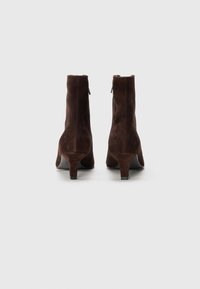 Bottines en suède marron avec un design effilé, fermeture éclair et un talon bas carré. La surface a une texture douce et des coutures sans couture.