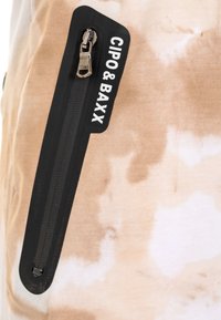 Light brown tie-dye fabric features a black zippered pocket. The pocket has a metallic zipper and the branding "CIPO & BAXX" in white.