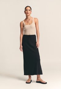 Beige geripptes Tanktop, schwarzer knöchellanger Rock mit elastischem Bund, minimalistische flache Sandalen. Glatte Textur, einfaches Design, keine Muster.