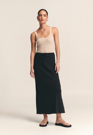 Top de tirantes de canalé beige y falda maxi negra con cintura elástica. La modelo lleva sandalias planas y está de pie sobre un fondo claro.