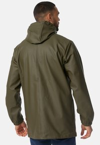 Jachetă impermeabilă de culoare verde măsliniu, cu glugă, manșete elastice și o textură netedă și elegantă. Dispune de o cusătură centrală care se întinde pe spate.
