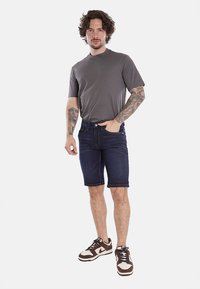 T-shirt grigio a maniche corte, pantaloni corti in denim blu scuro e sneaker atletiche marroni. I pantaloni corti in denim presentano una vestibilità classica e cinque tasche.