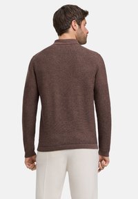 Brauner, gestrickter Pullover mit langen Ärmeln, strukturiertem Gewebe und gerippten Bündchen und Saum, von hinten gesehen. Auch neutrale Hosen sind sichtbar.