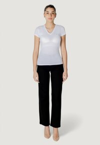 T-shirt bianca a V con maniche corte, realizzata in materiale leggero, abbinata a pantaloni neri a gamba larga e tacchi color nude.