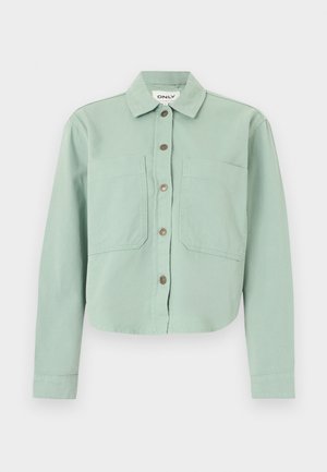 Chemise verte courte avec un col à revers, deux poches avant et une fermeture à boutons. Confectionnée dans un tissu texturé avec une finition douce.