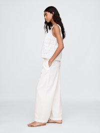 Hvit broderte bluse med bølget kant, kombinert med løse hvite bukser. Sandalene har tynne stropper. Glatt og lett stoff.
