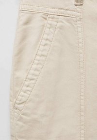 Beige katoenen shorts met een zijzak en zichtbare stiksels. De stof heeft een gladde textuur met een lichte glans.