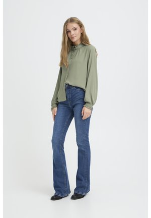 Hellgrüne Bluse mit Rüschenkragen, Knopfverschluß und langen Ärmeln, kombiniert mit blauen Schlagjeans und schwarzen Stiefeletten.