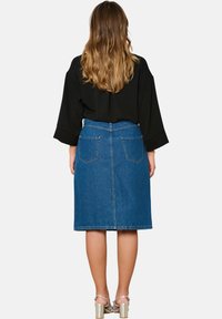 Denim A-linijska krila s srednje visokim pasom, zadnjimi žepi in surovim robom, v kombinaciji s črnim zgornjim delom in srebrnimi sandali s blok peto.