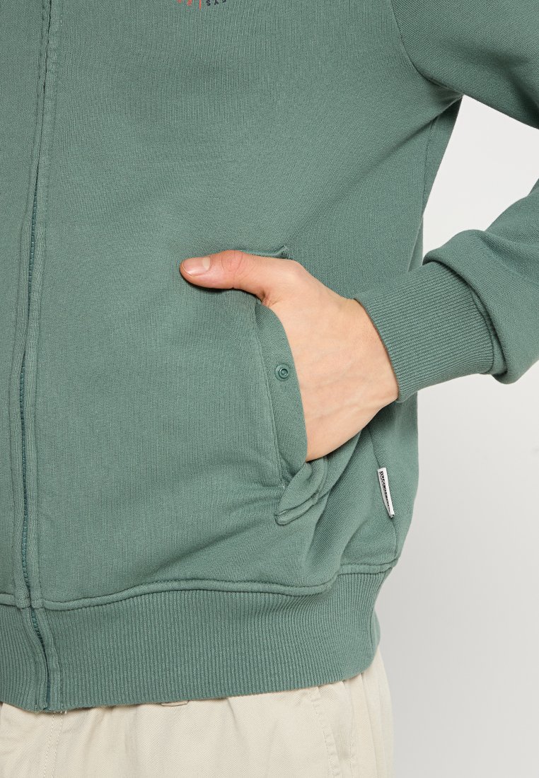 Felpa verde con zip, maniche a costine e fondo a costine, tessuto testurizzato, tasche laterali e un piccolo logo sul petto.