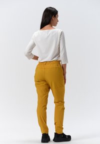 Gula byxor i ett ventilerande material med elastisk midja, matchade med en enkel vit långärmad överdel. Svarta skor synliga.