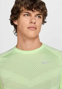 Svetlozelené športové tričko s textúrovaným vzorom, krátkymi rukávmi a strieborným logom Nike na hrudi. Dizajn z priedušného materiálu.