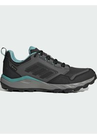 Zapato deportivo negro con parte superior de malla, acentos grises, detalles en teal y una suela texturizada para agarre. Incluye cordones y una pestaña en el talón.
