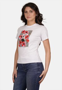 T-shirt bianco in cotone con una stampa floreale colorata su uno sfondo a righe bianche e nere, design aderente e maniche corte.