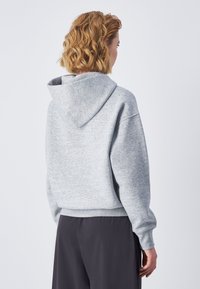 Sudadera con capucha gris de corte relajado, con costuras visibles, dobladillo y puños acanalados. Material acogedor. Vista desde la parte trasera.