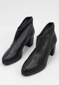 Black faux leather ankle boots with a pointed toe and a high block heel. Features a seamless design and visible stitching detail.