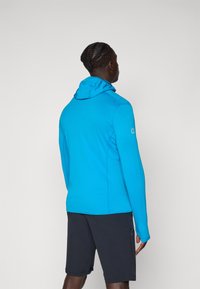 Kék, textúrázott kapucnis pulóver, testre szabott fazonnal és kapucnival. Sötét sorttal párosítva, amelyeken oldalsó zsebek találhatók, és egy diszkrét logó a mandzsettán.