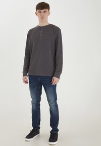 Cămașă henley gri cu mâneci lungi și trei butoane la guler, asortată cu blugi albaștri și adidași negri, având un design slim fit.