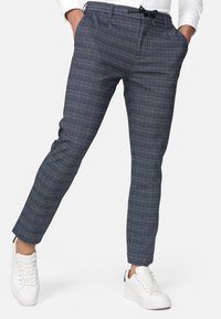 Marineblaue Karottenhose mit entspannter Passform, elastischem Bund und Kordelzug. Kombiniert mit weißen Sneakers, die einen modernen, lässigen Look zeigen.