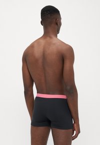 Boxeri negri cu o talie roz, având un design neted și strâns, dintr-un material moale, văzuți din spate.