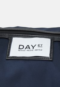 Marineblaue Stofftasche mit einem schwarzen Lederreißverschluss. Mit einem weißen Etikett mit schwarzem Text: "DAY ET RETHINK - RELOVE - RECYCLE."