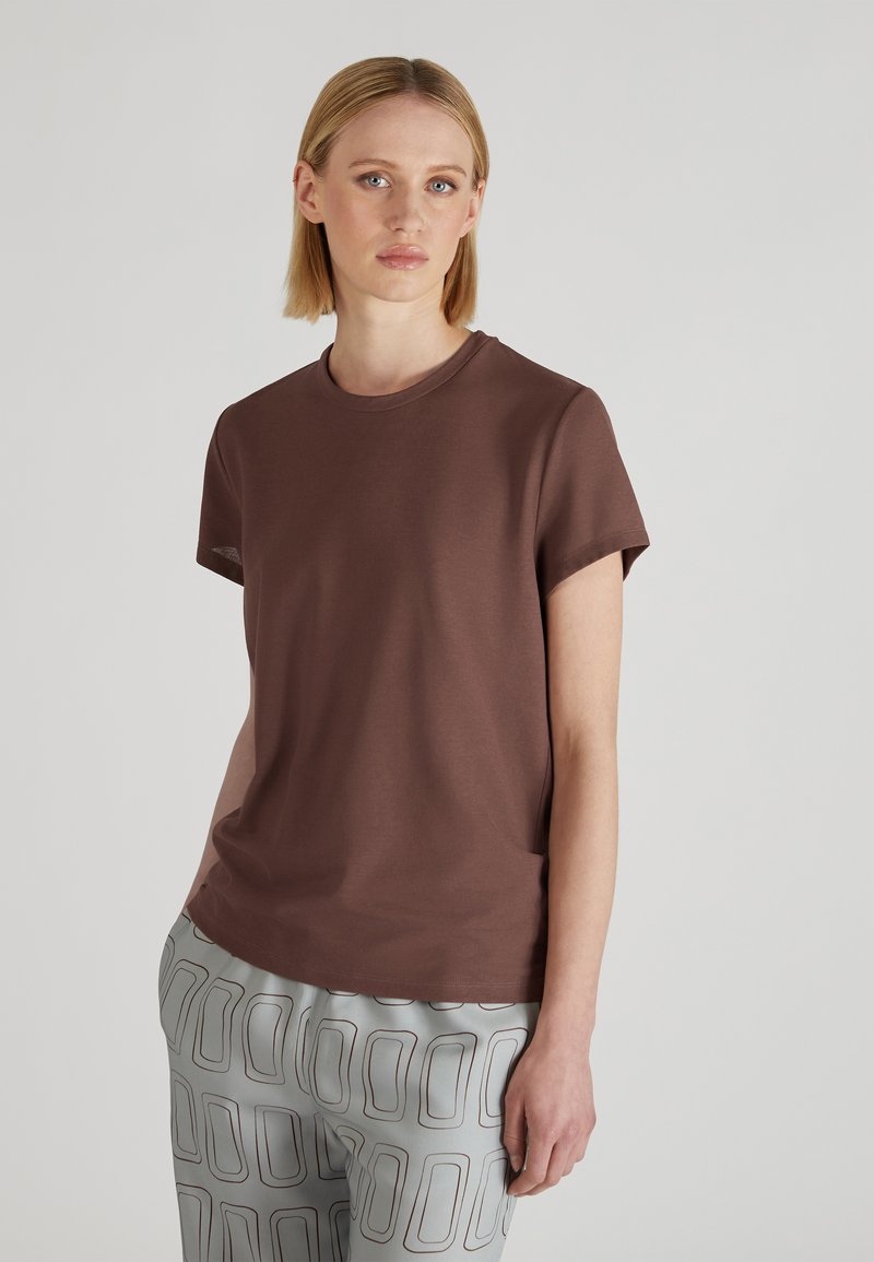 Brązowa koszulka z krótkim rękawem z gładkiego materiału z okrągłym dekoltem, sparowana z szarymi spodniami o wzorze w konturowe prostokąty.