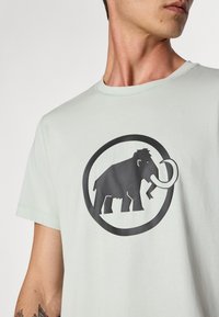 Light green cotton t-shirt featuring a black graphic of a mammoth within a circle. Soft texture with a classic crew neckline.