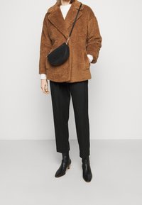 Giacca in pelliccia sintetica marrone con bavero, abbinata a pantaloni neri su misura e stivaletti neri. Include una borsa a tracolla rotonda nera.