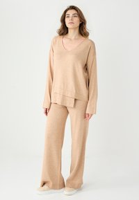 Maglione beige a maniche lunghe con scollo a V e pantaloni larghi abbinati, realizzati in morbido tessuto testurizzato, con un taglio rilassato e cuciture minime.
