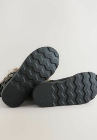 Suela de calzado negra con un patrón texturizado en zigzag, que presenta profundos relieves para tracción. Acento de piel de pelo suave a lo largo del borde superior.