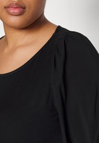 Top nero con scollo rotondo e maniche corte a sbuffo. Tessuto morbido e leggero con una consistenza liscia. Nessun motivo o accessori visibili.