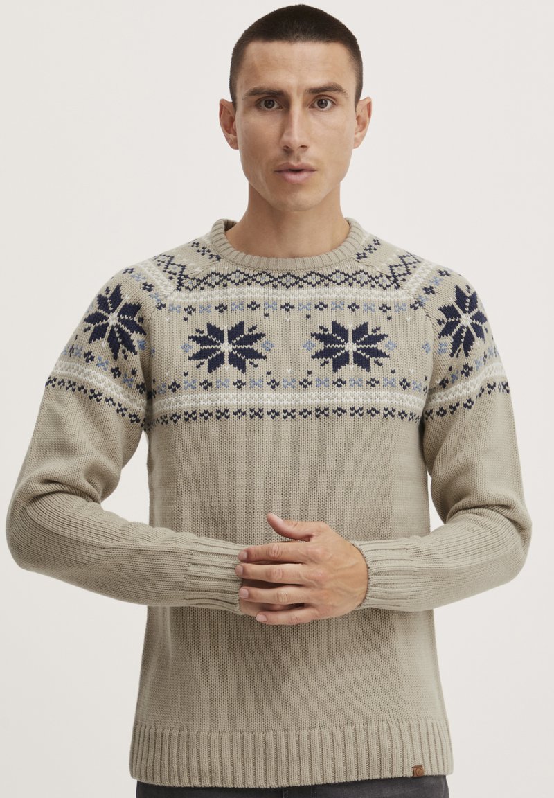 Pull en tricot de couleur beige clair, mettant en avant un empiècement à motifs avec des designs floraux bleus. Manches et bas côtelés, tissu texturé.