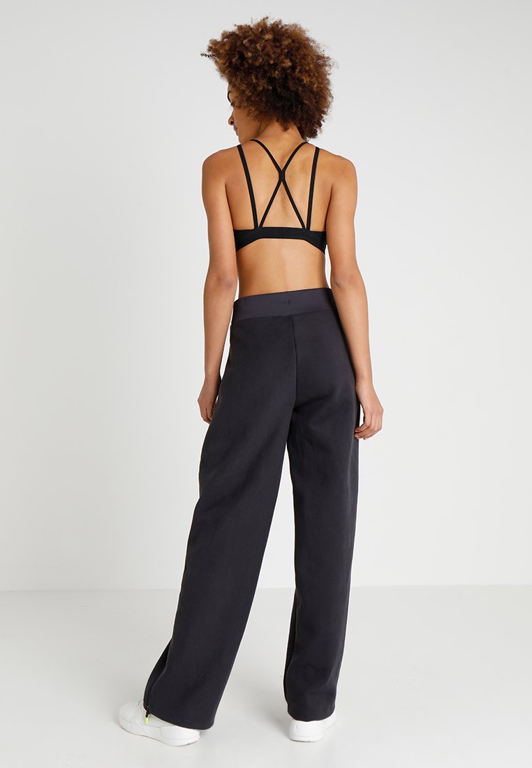 Soutien-gorge de sport noir à bretelles associé à un pantalon noir à taille haute, ample, en tissu lisse et sans motifs visibles.